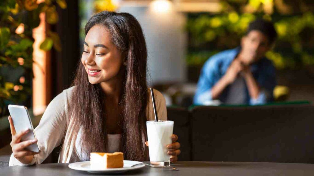 Online dating is driven by appearances (picture of women smiling on her phone watched by a guy from a distance)